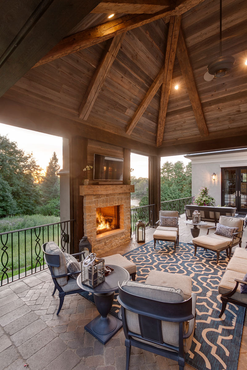 Covered patio with exposed wood beam ceiling, a stone fireplace and inviting patio furniture.