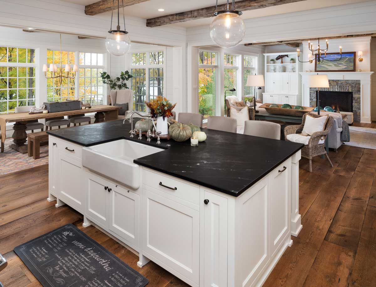Open floor plan great room viewed from the large kitchen with an expansive kitchen island, exposed ceiling beams and wide plank wood floors.