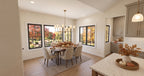 Alder Glen dining room with a round table, upholstered chairs, a brass chandelier and windows overlooking autumn trees.