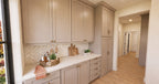 Alder Glen prep kitchen with gray cabinets, a pale countertop, brass knobs and a herringbone tile backsplash.
