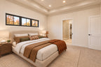 Primary bedroom with a high window above the upholstered bed, warm neutral bedding and an open bathroom doorway.
