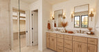 Alder Glen primary bathroom with a light wood double vanity, brass-framed mirrors and a doorway to the walk-in closet.