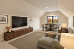 Bonus room with a green sectional, wall-mounted television, wood console and a game table beneath the far window.