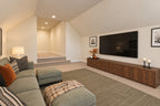 Bonus room with a green sectional facing the television and wood console beside steps to the entry landing.