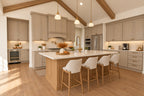 Kitchen with a wood island, four upholstered stools, taupe cabinetry, brass fixtures and a herringbone backsplash.