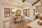Dining room with an oval wood table, upholstered chairs, a brass chandelier and windows overlooking autumn trees.