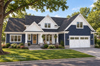 Front exterior of the Willow Cove modern farmhouse with navy siding, white gables, a covered porch and a two-car garage in summer.