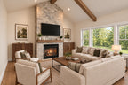 Willow Cove great room with a stone fireplace, cream sofas, wood armchairs and large windows beneath exposed ceiling beams.