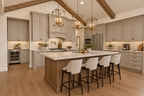 Willow Cove kitchen with a wood island, four upholstered stools, light cabinetry, brass lantern pendants and a herringbone backsplash.
