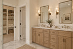 Willow Cove primary bathroom with a wood double vanity, framed mirrors, wall sconces and open shelving in the adjoining storage area.