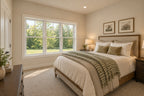Willow Cove front bedroom with a wood bed, neutral bedding, a green checked throw and a large window overlooking trees.