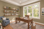 Oak Haven home office with a wood desk, floating shelves, a blue armchair and a blue patterned rug beside large windows.