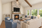 Oak Haven great room with a stone fireplace, cream sofas, blue armchairs and large windows beneath exposed ceiling beams.