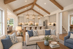 Oak Haven great room looking past cream sofas toward the kitchen island and lantern pendant lights beneath a vaulted wood-beam ceiling.