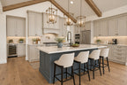 Oak Haven kitchen with a blue island, four upholstered stools, light cabinetry, brass lantern pendants and a herringbone backsplash.
