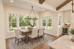 Oak Haven dining room with a rectangular wood table, cream upholstered chairs and a candle-style chandelier beside large windows.