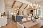 Oak Haven dining room looking across the wood table toward the blue kitchen island and great room, with a brass chandelier overhead.