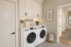 Oak Haven laundry area with a front-loading washer and dryer, white upper cabinets, a folding counter and a doorway to the hall.