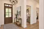 Oak Haven foyer with a wood-and-glass front door, geometric pendant and views into the powder room and bedroom hallway.