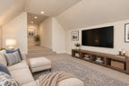 Oak Haven bonus room with a sectional sofa facing the television and wood media console, beside steps to the entry landing.