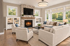 Great room with a stone fireplace, white built-ins and seating beside tall windows.
