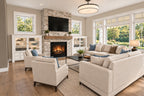 Great room with a stone fireplace, wood mantel, white built-ins and seating beside tall windows.