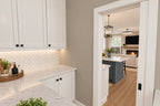 Walk-in pantry with white cabinets, a counter and herringbone backsplash, opening to the kitchen.