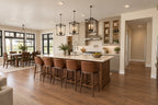 Kitchen island with a pale countertop and four stools, pendant lighting and a range wall beside the dining area.