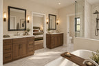 Primary bathroom with separate wood vanities, a freestanding tub and a glass shower, looking toward the bedroom.