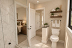 Upstairs bathroom with a glass shower, toilet, floating shelves and a doorway to the bedroom.
