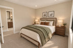Upstairs bedroom with a wood-framed bed, green throw, paired nightstands and an open doorway to the bathroom.