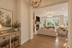 Foyer with a wood console, botanical artwork and a lantern pendant, opening to the great room fireplace and seating area.