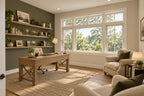 Home office/study with a wood desk, built-in shelves on a green accent wall, paired armchairs and a wide front window.