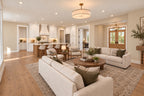 Great room seating around a round wood coffee table, looking toward the kitchen island, built-in shelving and wood entry doors.