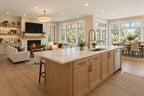 Kitchen island with a pale countertop and brass-tone faucet, looking toward the great room fireplace and window-lined dining area.