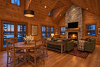 Family and dining room rendering with a vaulted wood ceiling, stone fireplace, green sofas and a round dining table.