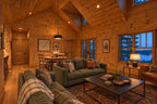 Family room rendering looking across green sofas and a coffee table toward the dining area beneath the vaulted wood ceiling.