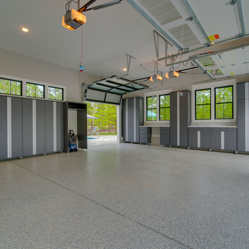 Custom home garage interior by Royal Oaks Design Inc with epoxy floor, gray storage cabinets, glass panel door, and transom windows