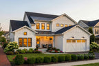 Stylish white farmhouse style home with black roof, a metal roof over the covered front porch and 2-car garage, surrounded by well-maintained garden.