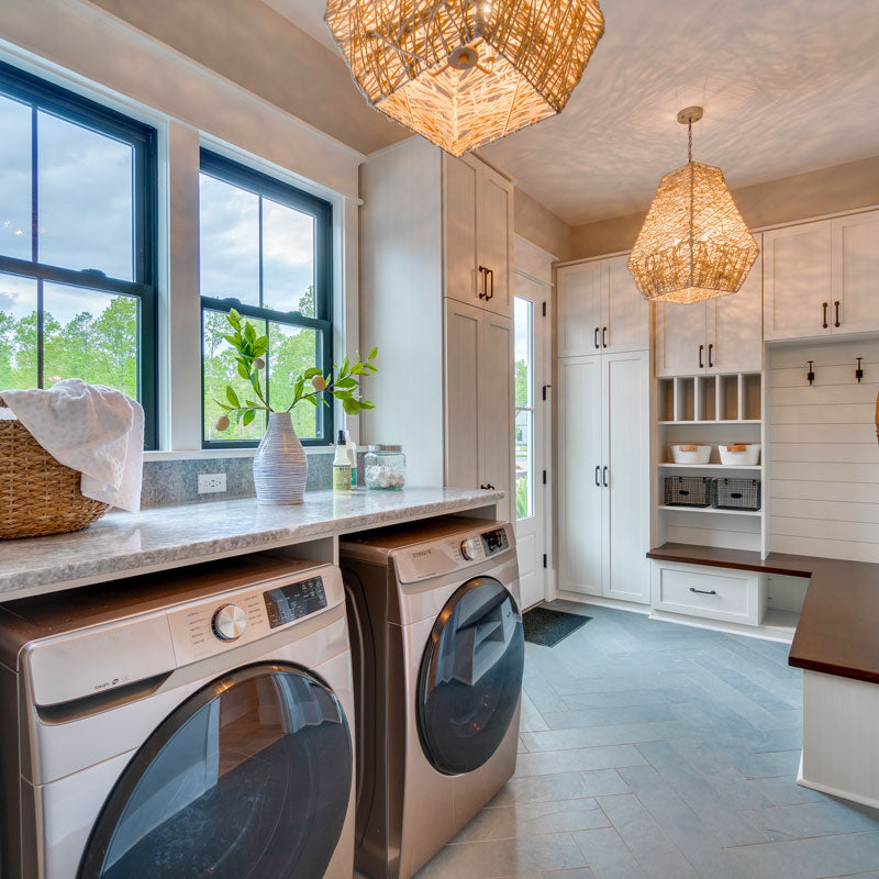 Farmhouse laundry room with front-load washer and dryer, stone countertop folding station, white shaker cabinets, woven pendant lights, and mudroom built-ins